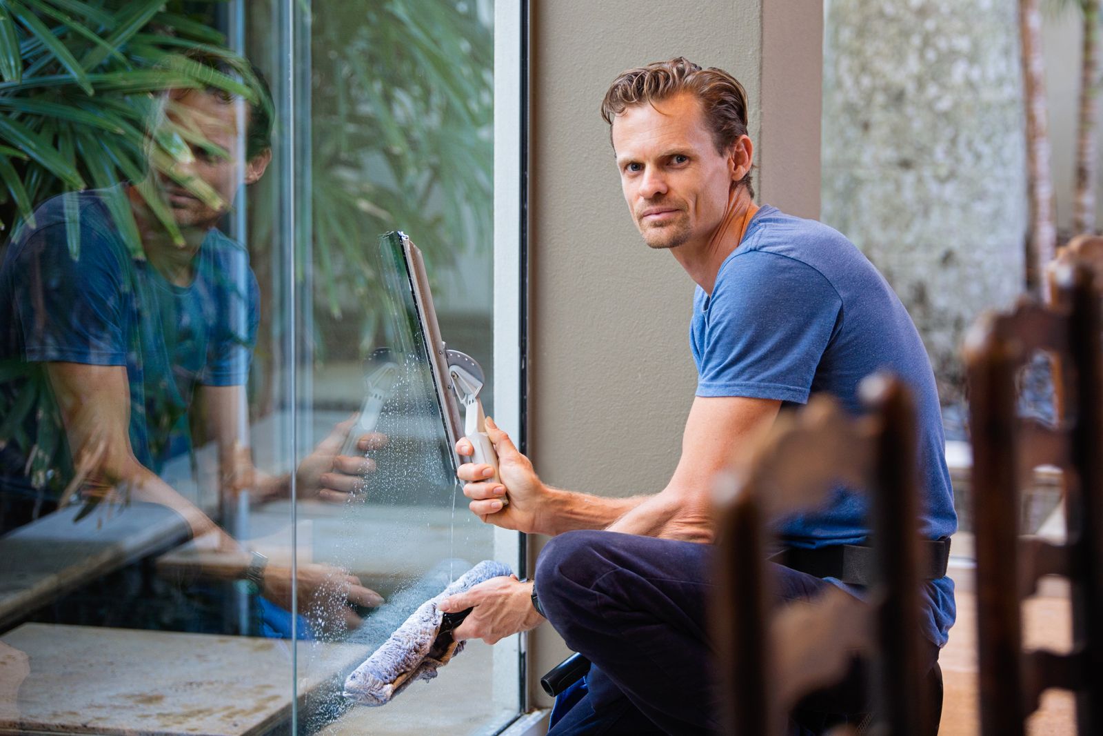 A Majestic window cleaner using a squeegee on a residential glass door, water sheeting cleanly off the pane
